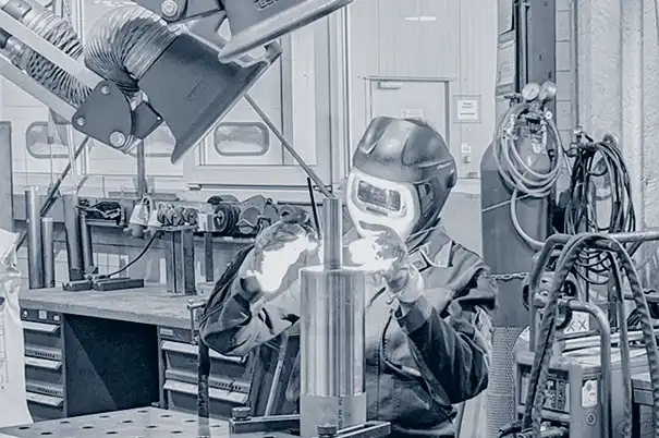 Eine Person mit Schweißhelm verwendet in einer Industriewerkstatt einen Schweißbrenner auf Metall.